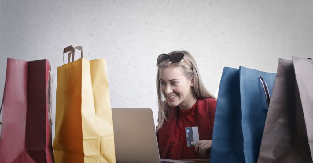 A joyful woman shopping online using a laptop with colorful shopping bags surrounding her.
