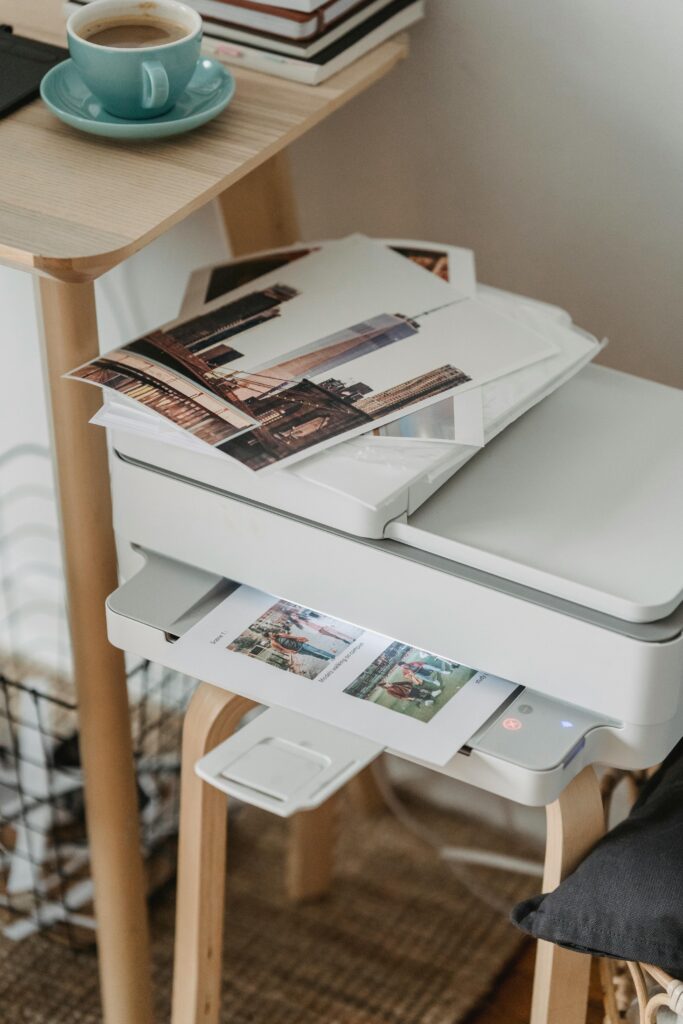 A cozy home office corner with a printer, coffee cup, and printed photos on a wooden table.